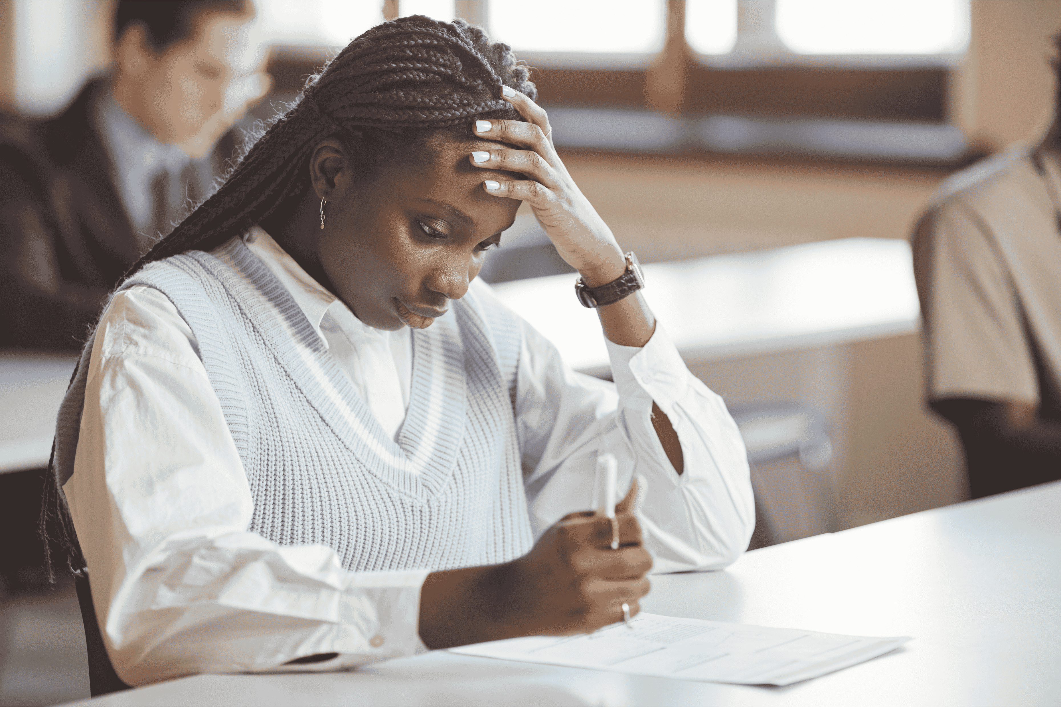 A young Black woman with her head in her hand while taking a test, looking concerned.